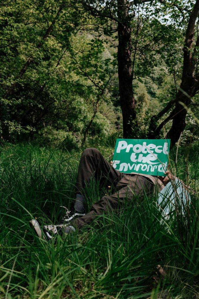 A man lies in the grass holding a 'Protect the Environment' sign.