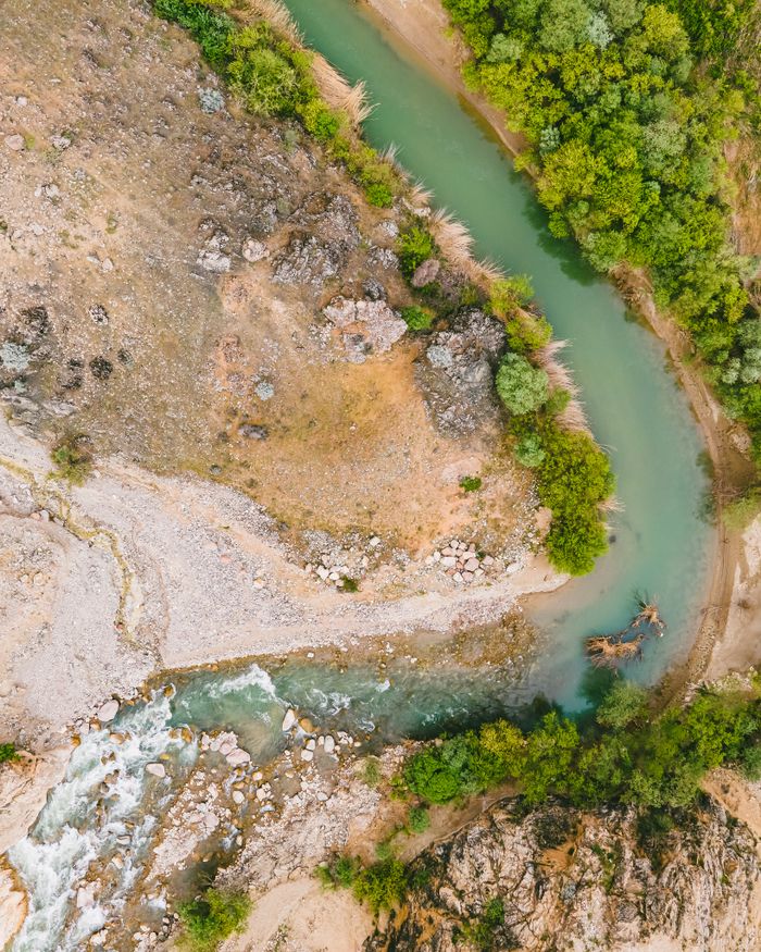 Aerial shot of a winding river cutting through a mountainous terrain with lush vegetation.