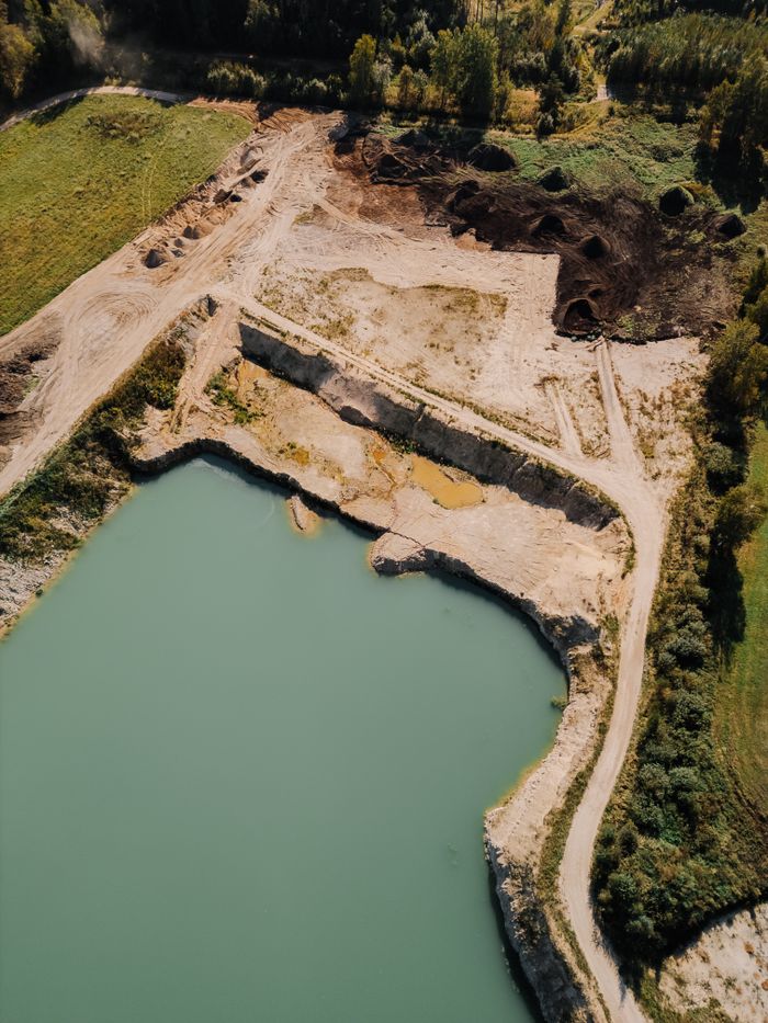 Aerial shot of a quarry with turquoise water in Latvia, showcasing land excavation and nature.